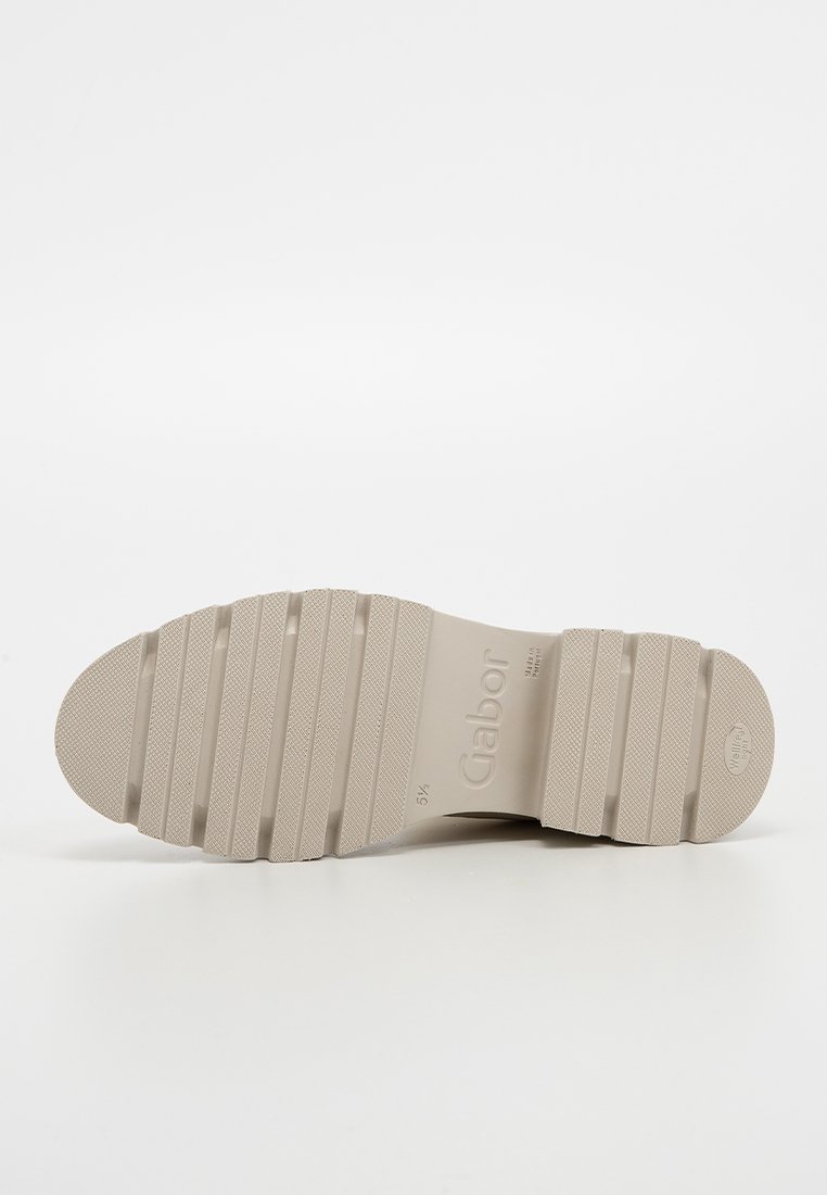 Beiger Gummischuhsohle mit gerippter Textur und geprägtem Branding. Entwickelt für Grip und Langlebigkeit. Flach mit runder Zehenform.