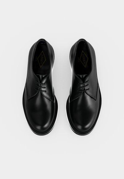 Ζευγάρι γυαλισμένα μαύρα δερμάτινα παπούτσια με κλειστή κορδόνι, στρογγυλεμένα δάχτυλα και ελάχιστο ράψιμο, εμφανίζονται από πάνω σε λευκό φόντο.