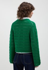 Maglione verde a maglia con un motivo a righe testurizzato, colletto rotondo e maniche lunghe, abbinato a jeans in denim scuri.