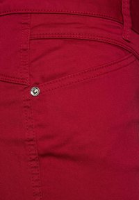 Red cotton blend pants featuring a front pocket with a silver button, visible stitching, and a smooth texture.