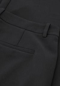 Zwarte broek van gladde stof. Heeft een vlakke voorkant, riemlussen en een enkele achterzak met minimale stikdetails.