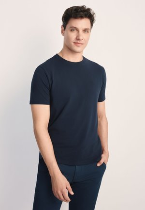 Granatowy bawełniany t-shirt z okrągłym dekoltem i krótkimi rękawami. Gładka faktura, minimalistyczny styl, z małym logo na piersi.