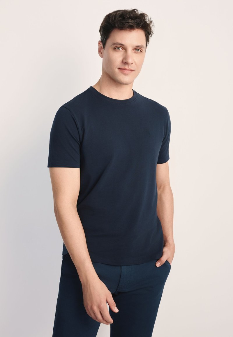 Granatowy bawełniany t-shirt z okrągłym dekoltem i krótkimi rękawami. Gładka faktura, minimalistyczny styl, z małym logo na piersi.