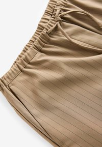 Pantaloni corti a righe beige con vita elastica e cordino. Texture liscia e tasche laterali, con sottili righe nere.