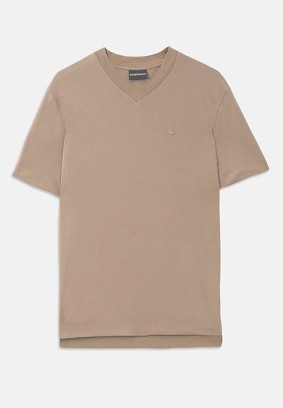 Camiseta de color beige de manga corta con escote en V, con un pequeño emblema de logo en el lado izquierdo del pecho, hecha de suave tejido de algodón.