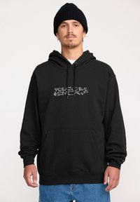 Hoodie noir en tissu épais, avec une poche kangourou �à l'avant et un logo emblématique en argent. À associer avec un pantalon en denim bleu.