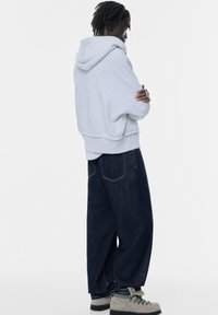 Grå kort hoodie med huva, tillsammans med mörkblå löst sittande denimbyxor. Anmärkningsvärda grå skor med textur och gröna detaljer.