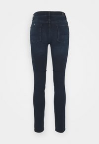 Jeans skinny em denim azul escuro, com cintura média, pernas ajustadas e dois bolsos traseiros com detalhe de costura curva.