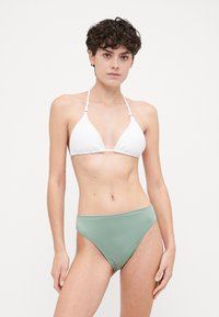 Balta tekstūruota trikampio formos bikini viršutinė dalis derinama su aukšta juosmens ribota žalia bikini apatine dalimi, su reguliuojamomis petnešomis ir lygiu paviršiumi.