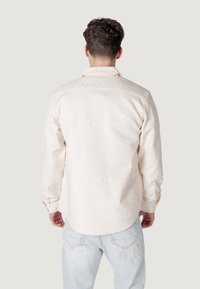 Camicia a maniche lunghe in crema chiaro, con un motivo sottile. Collo button-down, polsi singoli e dettaglio dell'orlo arrotondato.