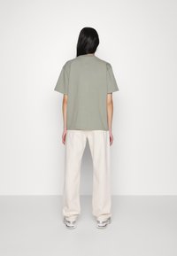 Vapaa-ajan löysämallinen vaaleanvihreä puuvillainen t-paita lyhyillä hihoilla, yhdistetty vaaleanharmaisiin leveälahkeisiin housuihin ja lenkkareihin. Yksinkertainen ja selkeä muotoilu.