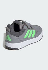 Zapatilla deportiva gris con detalles en verde, que cuenta con una parte superior sintética suave, forro de malla transpirable y cierre de velcro.