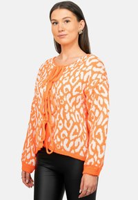 Cardigan lavorato a maglia arancione con stampa leopardata bianca, presenta una scollatura a boat, maniche lunghe e dettaglio centrale con lacci. Tessuto testurizzato.