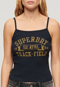 Débardeur côtelé bleu marine à fines bretelles avec le texte doré "SUPERDRY TRACK-FIELD" et un détail de logo. Ourlet ajusté au niveau de la taille.