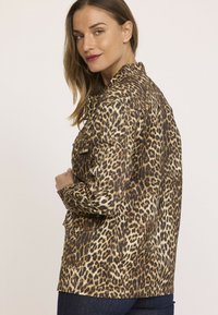 Veste à imprimé léopard avec un design à col, fermeture à boutons et deux poches avant. Présente une palette de couleurs brun et crème avec un tissu texturé.