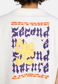 White cotton t-shirt featuring colorful graphics with a yellow cartoon dog and bold, stylized text in purple and red.