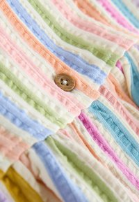 Detail viacfarebnej pastelovej rebrovanej látky so zašitým hnedým okrúhlym gombíkom uprostred.