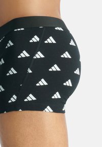 Svarta boxer underkläder i bomull, med ett upprepat vitt triangelmönster och en enfärgad svart midja. Tätt sittande design.