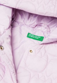Helllila gesteppte Jackeninnenseite mit glatter Textur, ausgestattet mit einem grünen Label "United Colors of Benetton" und goldenen Druckknöpfen.