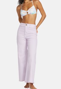 Vaqueros de pierna ancha de color lila claro con bajo deshilachado, diseño de cintura alta y cierre con botón dorado. Llevados con un top de bikini halter colorido.