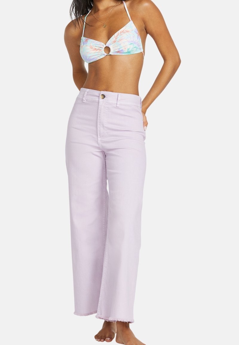 Vaqueros de pierna ancha de color lila claro con bajo deshilachado, diseño de cintura alta y cierre con botón dorado. Llevados con un top de bikini halter colorido.