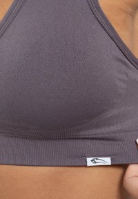 Grijze geribbelde bralette met een gladde textuur, voorzien van een merklabel detail in het wit aan de onderkant en een diep uitgesneden halslijn.