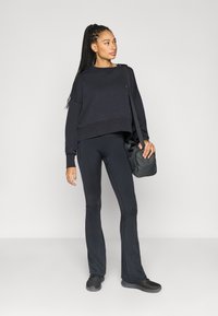 Μαύρο cropped φούτερ με ριμπ μανσέτες, σε συνδυασμό με μαύρο κολάν με φαρδιά παντελόνια, διακοσμημένο με μικρό λογότυπο, και συνοδευόμενο από μαύρη τσάντα χειρός.