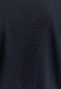 Tissu sombre avec un grand chiffre 7 cousu dans une nuance légèrement différente de couleur foncée.