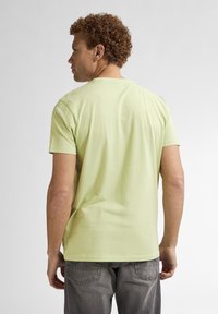 T-shirt verde menta a maniche corte in una vestibilità rilassata, con colletto tondo e texture in cotone morbido, abbinato a jeans grigi.