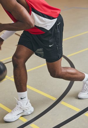Mustat verkkokankaiset koripallosortsit, joissa on valkoisia yksityiskohtia ja Nike-logo. Yhdistetty valkoisiin urheilukenkiin ja nilkkapituisille valkoisille sukille.