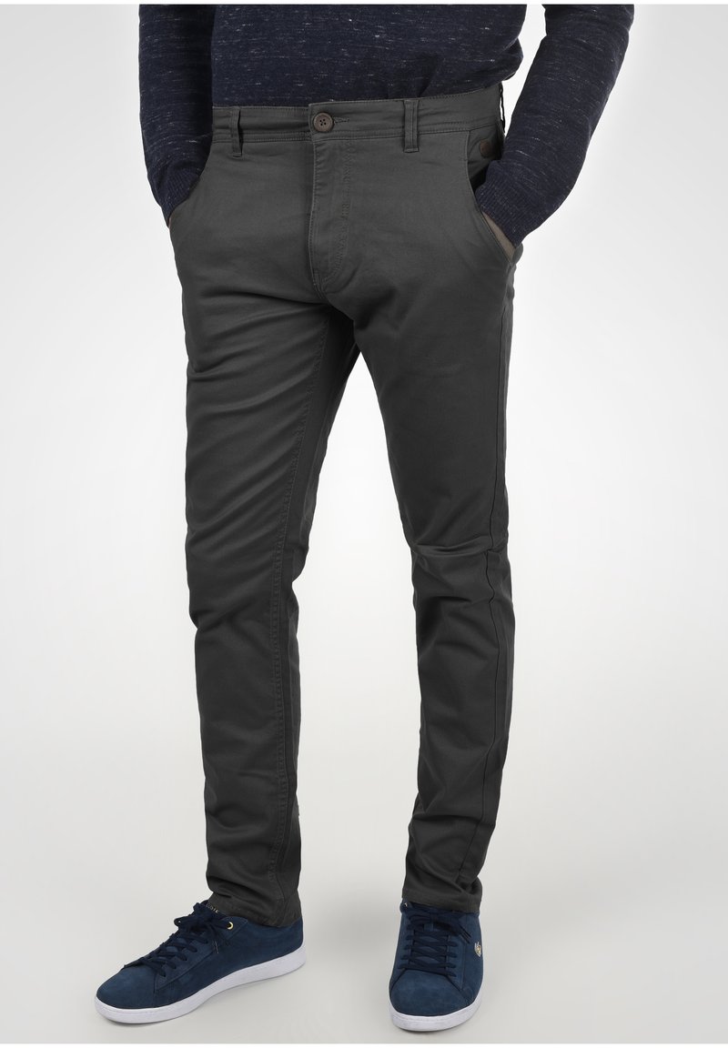 Pantaloni slim-fit grigio scuro realizzati in tessuto misto cotone, con chiusura a bottone, tasche e dettagli testurizzati sottili. Indossati con sneakers blu navy.