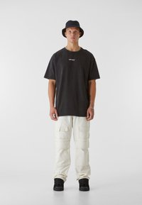 Black oversized t-shirt with white text, cream cargo pants with multiple pockets, and black high-top sneakers, set against a neutral background.