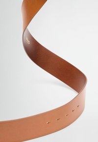Tan læderbælte med en glat overflade, der har et slankt design, synlige huller til justeringer, og prægede logo detaljer.