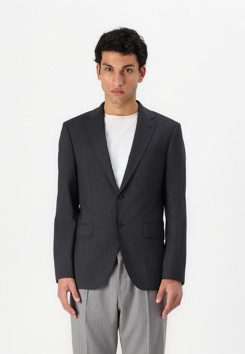 Mörkgrå blazer med två framknappar, slagkragar och en bröstficka. Buren över en ljusfärgad t-shirt och kombinerad med randiga byxor.