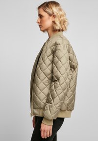 Quilted khaki bomberjakke med glidelås foran, ribbestrikkede mansjetter og kant. Har en klassisk passform og teksturert overflate for varme.