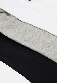 Drei Paar Socken in Weiß, Grau und Schwarz, aus weichem, dehnbarem Stoff mit glatter Textur und gerippten Bündchen.