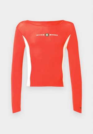 Czerwony sportowy top z długim rękawem z białymi akcentami i okrągłym dekoltem. Na środku znajduje się logo "NIKE SHOX", a na rękawie znak Nike.