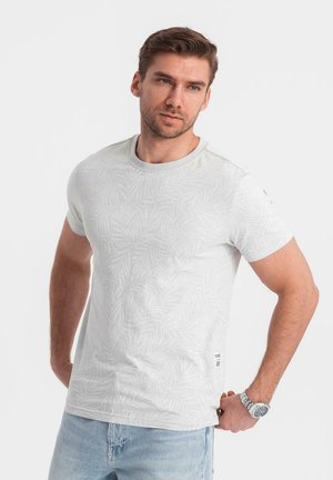Camiseta blanca de manga corta con un sutil estampado de hojas, cuello redondo y material suave. Combinada con jeans de color azul claro.