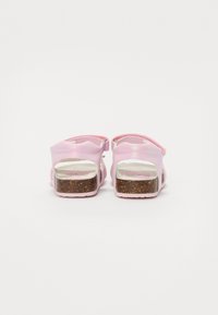 Rosa sandaler med en blank overflate, justerbar stropp, og en teksturert brun plattformsåle. Bakvisning som viser utskjæringsdesign.