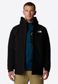 Zwarte waterdichte jas met capuchon, voorzien van een ritszak op de borst, neon groene ritsaccent en logo op de linkerkant van de borst.