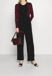 Bordowy kardigan na czarnym topie, połączony z czarnymi spodniami o szerokich nogawkach. Uzupełniony fakturowaną bordową torebką i czarnymi sandałami na obcasie.