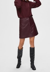 Burgundy leather A-line skirt with front buttons and clean lines, paired with a matching blouse and black knee-high boots.