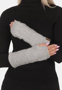 Guanti senza dita grigi in maglia, con polsini a costine, una texture morbida e un piccolo dettaglio in pelle. Indossati sopra un dolcevita nero.