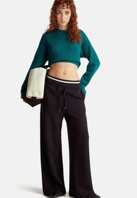 Turkusowy krótki sweter i czarne spodnie o szerokich nogawkach z troczkiem, z białym paskiem w paski w talii. Modelka trzyma torebkę w kolorze kremowym.