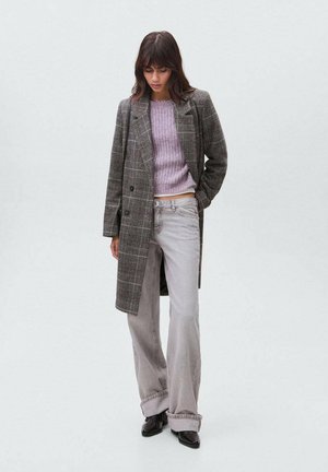 Manteau à carreaux gris, associé à un haut tricoté violet clair et à un jean évasé gris clair. Des chaussures noires complètent le look. Design minimaliste.
