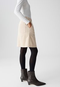 Beige corduroy rok met zijzakken, gedragen met zwarte panty en enkellaarsjes. De rok heeft een uitlopende vorm en een gestructureerd oppervlak.