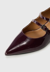 Burgundy lakkinahkakengät terävällä kärjellä, joissa on kaksi ohutta nilkkahihnaa soljella ja pehmustettu sisäpohja.