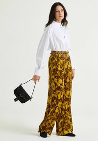 Camicia bianca con bottoni, pantaloni ampi a fantasia floreale gialla con vita arricciata, borsa nera testurizzata con nappina.