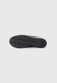 Semelle de chaussure avec une bande de roulement en caoutchouc noir présentant des rainures ondulées et droites sur un fond clair.