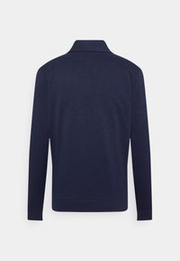 Polo de manga larga azul marino, con cuello con solapa y puños acanalados. Textura lisa con un diseño minimalista.